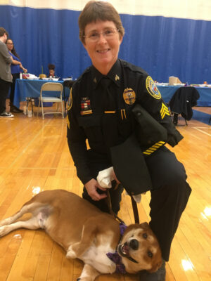 Lawrence Police officer in the gym kneeling next to a dog 