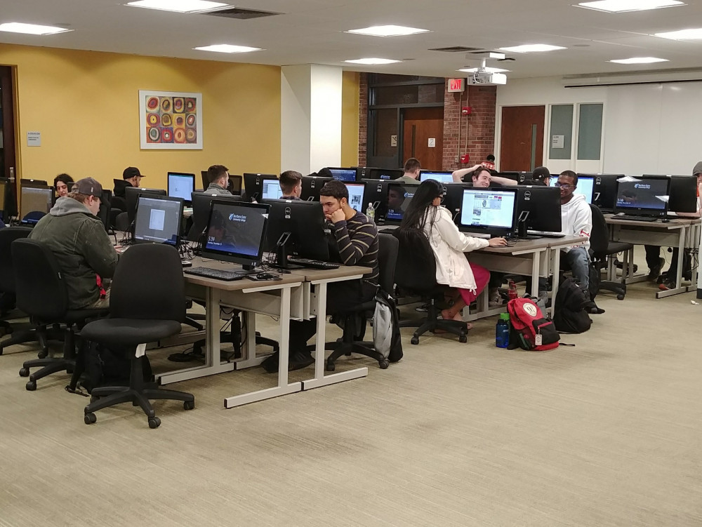 photo of rows of computers, and students doing work on them
