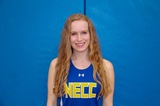 woman standing in front of blue background. She is wearing a necc sports uniform