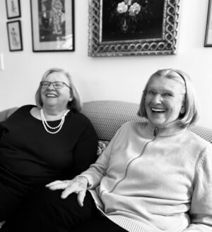 Two women sit next to eachother on a couch. 