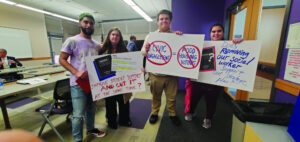 Faculty and students hold signs at a Board of Trustees meeting.