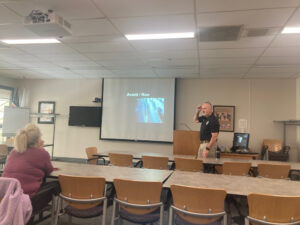 NECC Public Safety Officer Peter Sheldon stands in front of a classroom with desks and whiteboard in it. 