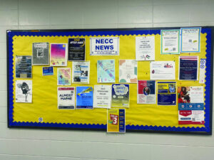 A bulletin board in a hallway with flyers on it. 