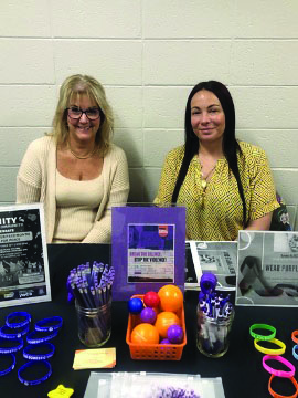Two women standing behind a table with informational books and posters on it. 