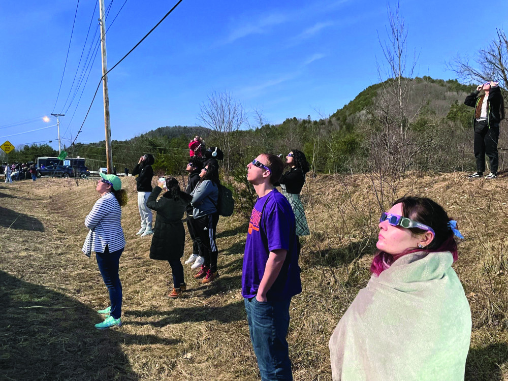 Students wearing eclipse glasses stand on a hillside in Vermont and look at the eclipse.