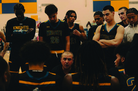 Men's basketball team members huddle around their coach.