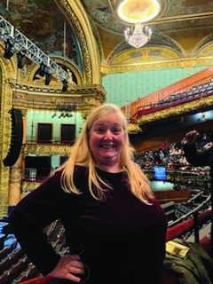 Woman stands and smiles in seats of theater.