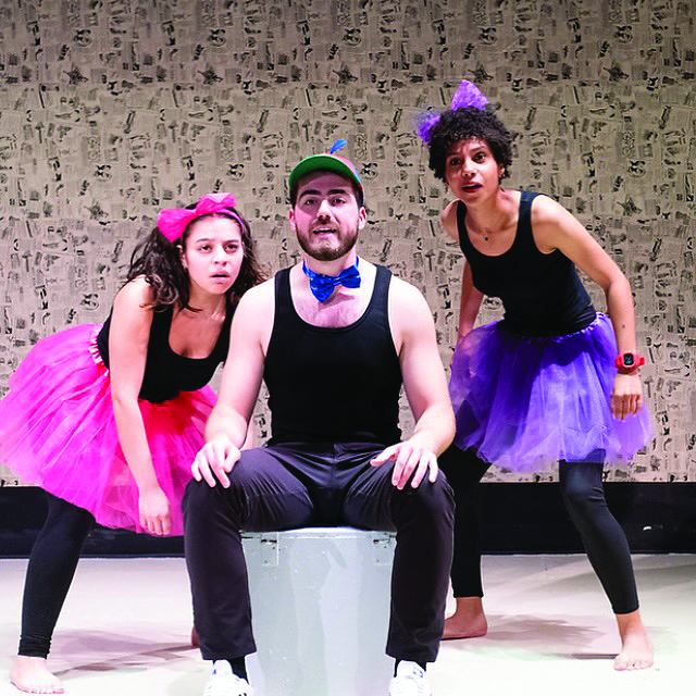 Two women wearing tutus and a man sitting a stool with a beanie.
