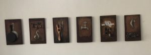 A series of artwork hanging on wall. Drawings or paintings of various objects. A faucet, a pan, and something that appears to be hooks and tongs.