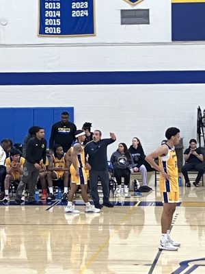 A basketball coach talks to a player on the court in between the action.