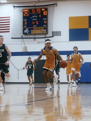A male basketball player runs down the court dribbling the ball.