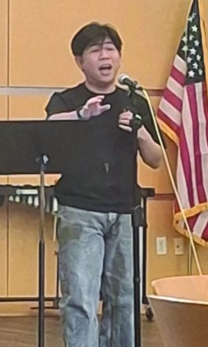 A man sings with a microphone in front of a music stand.