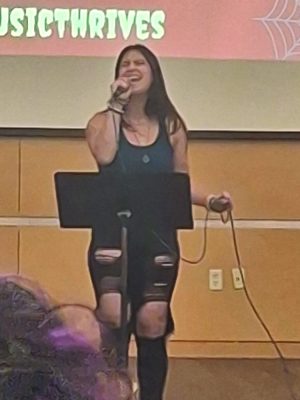 A woman sings while holding a microphone in front of a music stand.