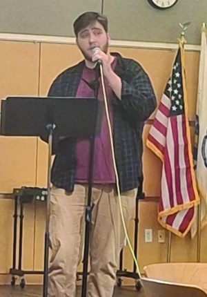 A man stands in front of a music stand and sings with a microphone.