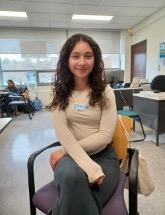 A woman sits in a chair in a classroom and smiles at the camera.