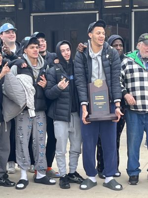 Members of the basketball team stand in a line holding their national championship trophy. 