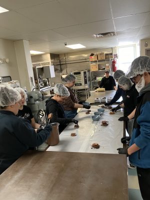 PACE TRIO staff on Van Otis chocolate factory tour. People stand around a table looking at chocolate.