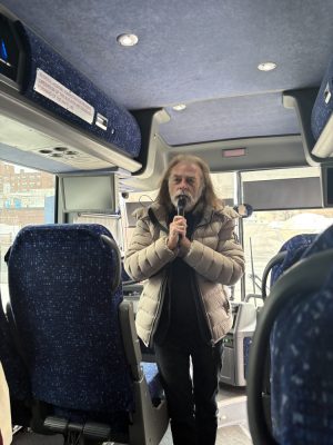 A man with a microphone speaks to a group of people on a bus. 