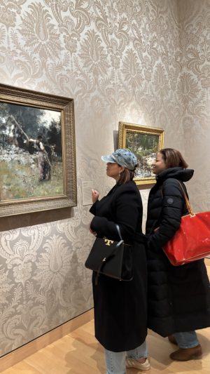 Two women stand in the Museum of Fine Arts and look at a painting on the wall. 