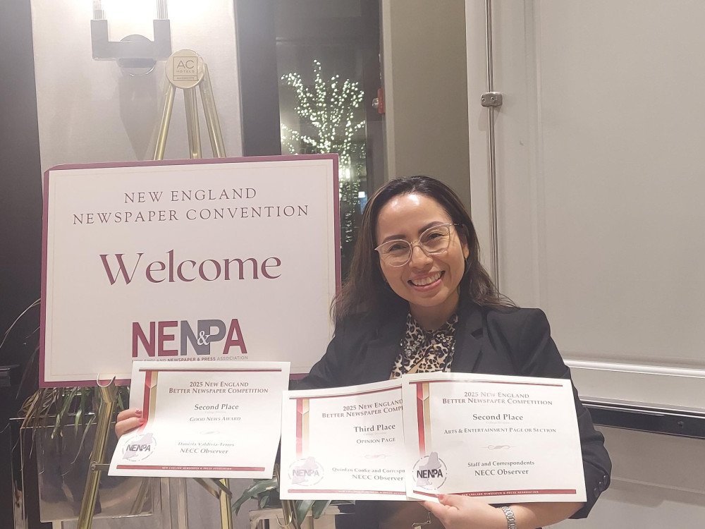 Woman stands with award certificates in front of a sign for NENPA