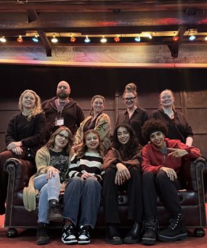 A group of men and women sit in a row of theater seats and stand behind them smiling. 