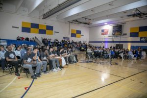 People sit in a row of chairs in the NECC gym