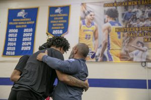 Basketball coach hugs two basketball players.