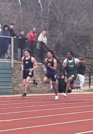 Three track runners are running on the track field. Two runners are from NECC